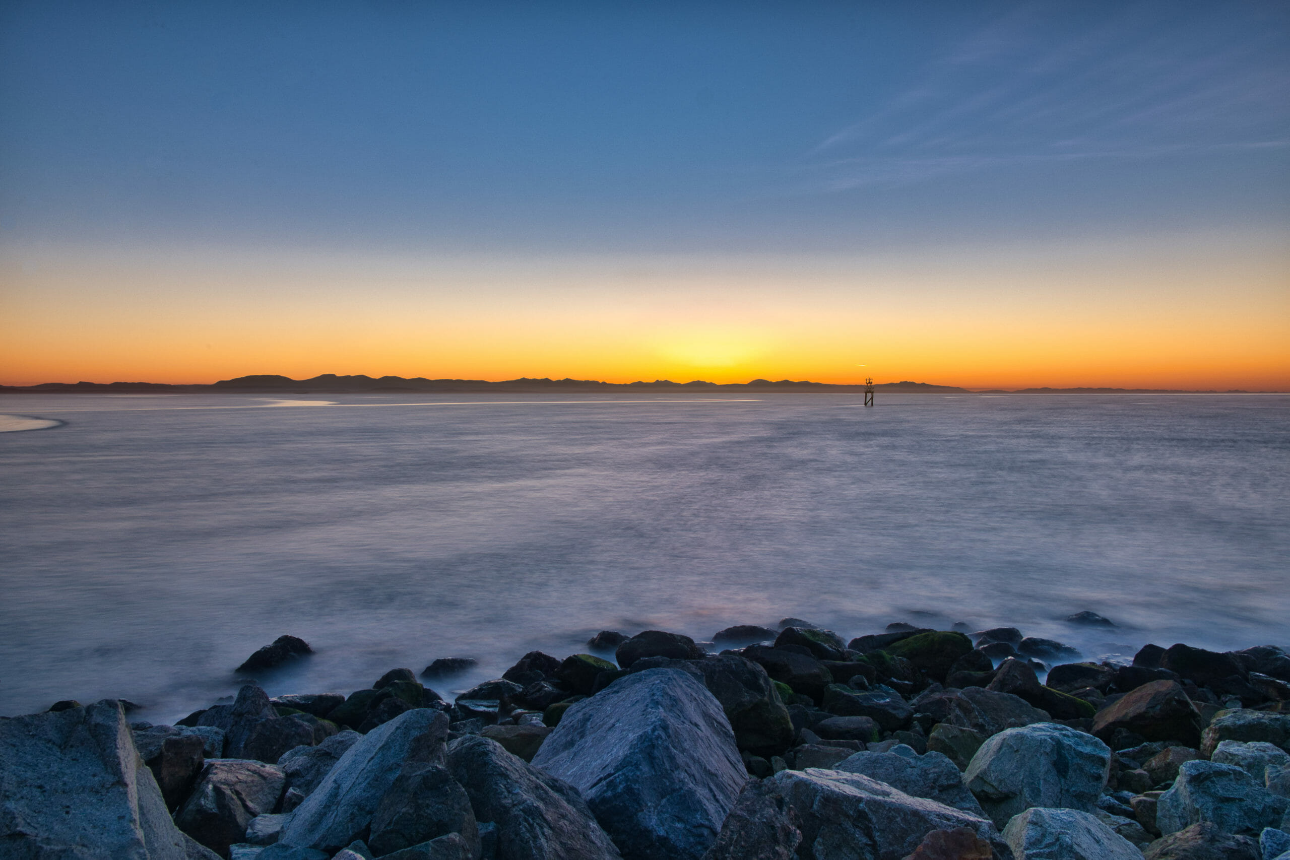 Long exposure of Georgia Strait at sunset with beautiful gradient sky orange to blue as seen from Terminus at Iona Beach