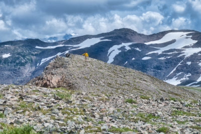 Male hiker standing on top of rocky ridge with mountains and stormy clouds at Panorama Ridge in Garibaldi Provincial Park