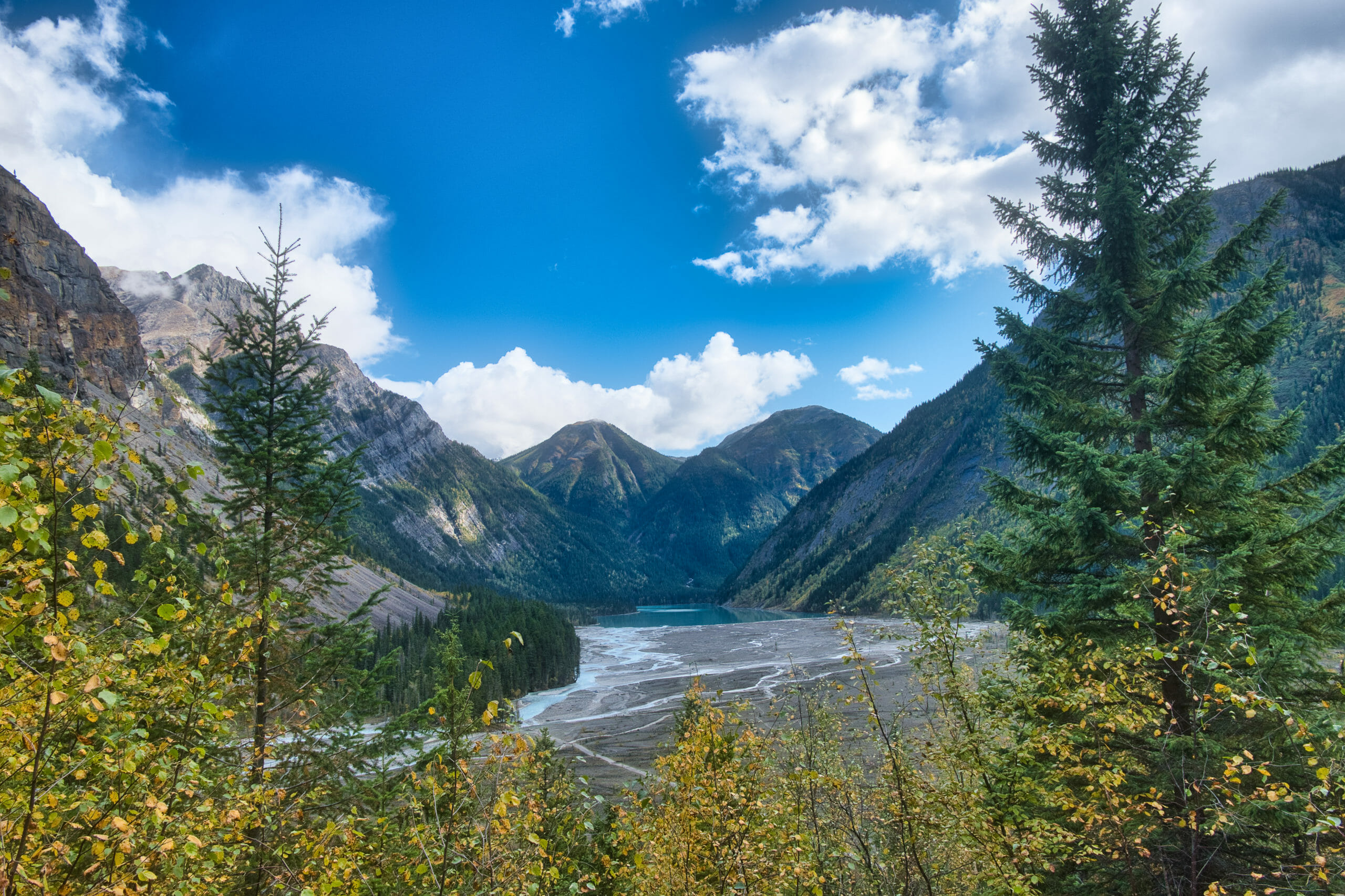 Edge of Kinney Lake in distance encapsulated by mountains on Berg Lake Trail in Mount Robson Provincial Park on sunny day