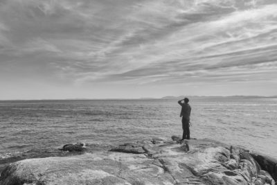 Male hiker at Lighthouse Park observing flying object in distance over Burrard Inlet and Vancouver shoreline in distance