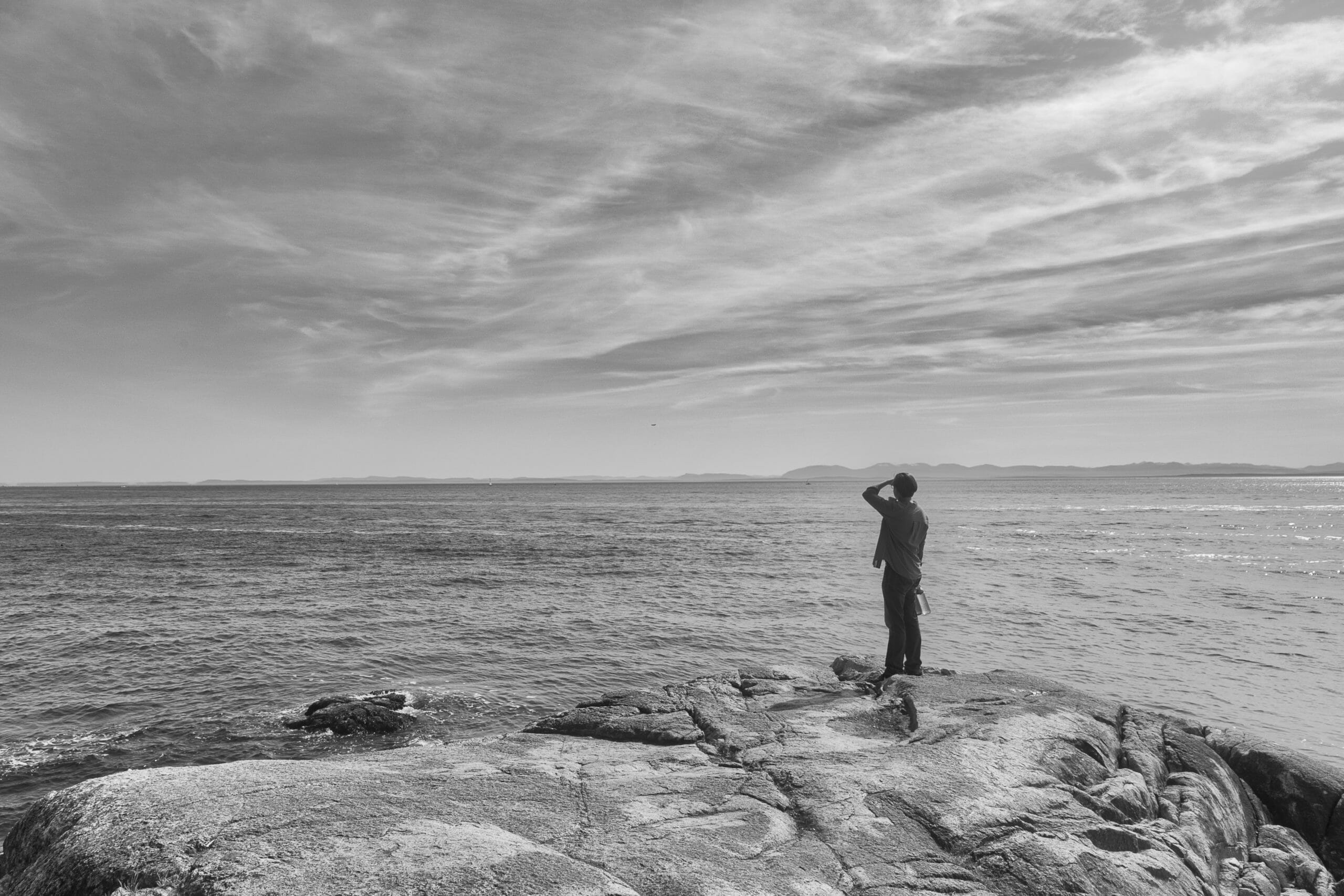 Male hiker at Lighthouse Park observing flying object in distance over Burrard Inlet and Vancouver shoreline in distance