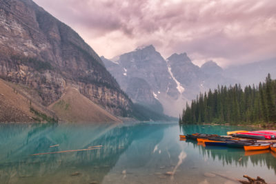 Moraine Lake as seen from Shoreline Trail in summer with smoky skies from wildfires and kayaks and canoes in the foreground