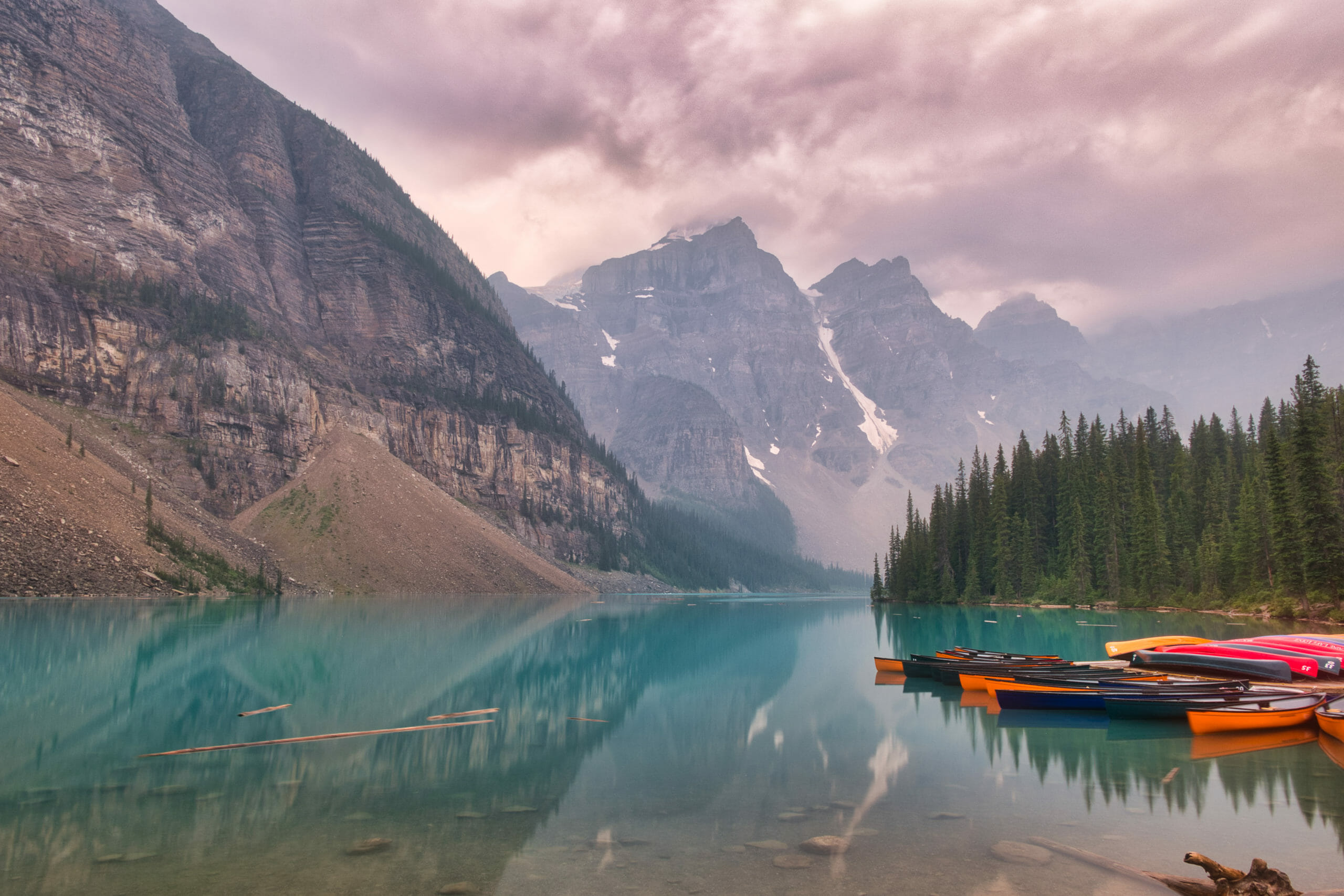 Moraine Lake as seen from Shoreline Trail in summer with smoky skies from wildfires and kayaks and canoes in the foreground