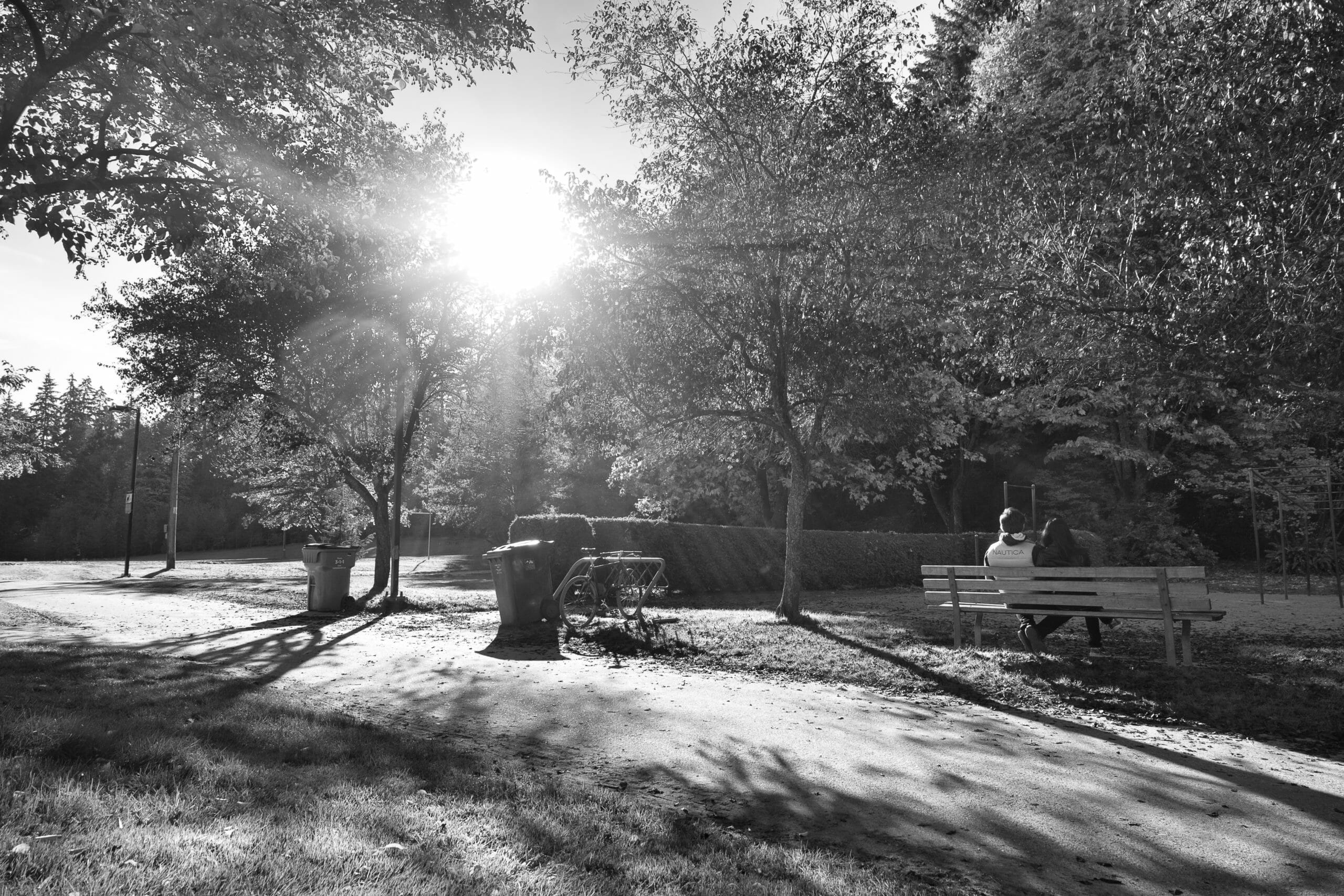 Couple sitting on park bench among fall foliage and blindingly bright sunlight shining down at Stanley Park