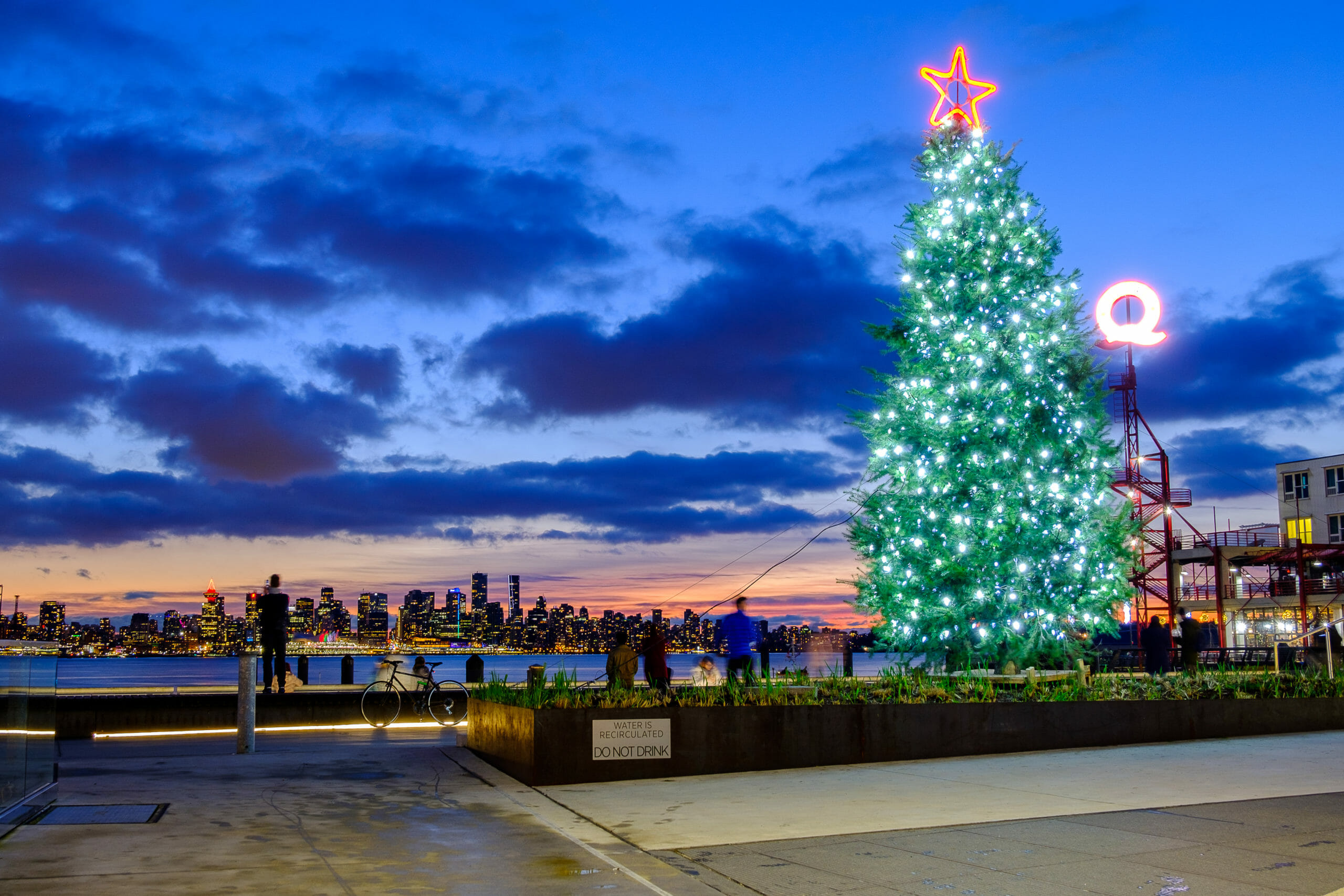 Long exposure of Christmas tree and pedestrians at Lonsdale Quay overlooking Vancouver Harbour and downtown skyline at dusk