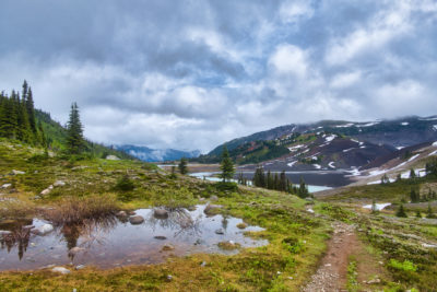 Storm clouds rolling over mountains and vegetation reflected in pond with alpine lake in Garibaldi Provincial Park